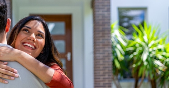 Couple joyfully embracing in front of a home.